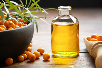 Wall Mural - Bottle of sea buckthorn essential oil, bowl of sandthorn berries, wooden scoop of sea buckthorn berries.