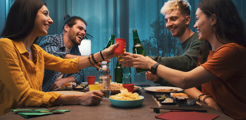 Happy friends toasting and eating together at home