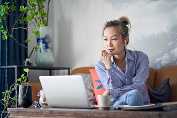 Wall Mural - mature asian woman working from home using laptop computer and cellphone