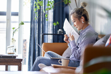 Wall Mural - mature asian woman stock photographer working at home using notebook computer