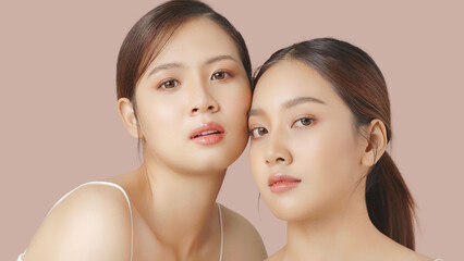 Close up portrait beauty shot of two young beautiful Asian girls looking at camera isolated on brown background.