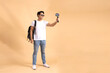 Young Asian tourist backpacker man smiling and taking a selfie and blog isolated on beige background