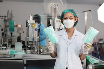 Poster - Worker woman in personal protective equipment or PPE inspecting showing quality of mask and medical face mask production line in factory, manufacturing industry and factory concept.