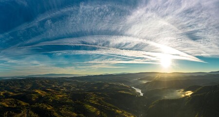 Aerial panorama view of a foggy sunrise with visible airplane contrails in a hilly area near Resita city, Romania. Captured with a drone