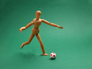 wooden figurine doll playing miniature toy football soccer ball black and white colour over green background copy text space concept