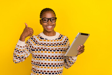 Wall Mural - Photo of funky satisfied girl with cornrows dressed print pullover showing thumb up hold tablet isolated on vivid yellow color background