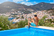 © moofushi - A tourist man sits by the swimming pool enjoys the view of the city at Poros island, Saronic Gulf, Greece, during summer time