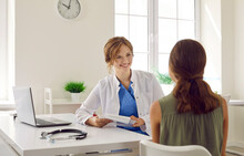 Friendly Doctor Talking To Her Young Patient. Happy, Smiling Woman Who Works As A General Practitioner Is Sitting At Her Desk And Giving A Medical Consultation To A Child. Medicine Concept