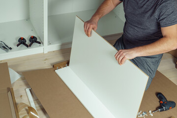 Wall Mural - Male hands hold and insert bottom of white drawer, assembling dresser or wardrobe on floor. Electric screwdriver and clamps lie by side. Self-assembly of furniture at home, DIY, furniture repair