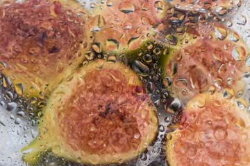 Fresh figs and fig halves on a plate under a film with drops of water. Dark background, close-up view from above.