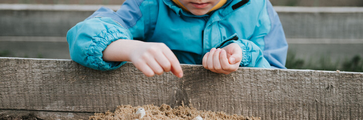 spring planting seeding in farm garden. little six year old kid boy farmer gardener plants and sow vegetable seeds in soil in bed. gardening and beginning summer season in countryside village. banner