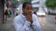 © Marco - One anxious black man standing in urban street feeling nervous and stressed. Desperate African American rubbing hands in anxiety in modern sidewalk