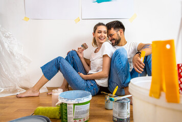 Young couple sitting on the floor choosing color for painting the wall in their home.