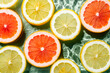 Colorful background image of fruit citrus lemon, orange, grapefruit, slices in water splashing fresh transparent surface with flecks. Flat lay, top view. Summer beach tropical