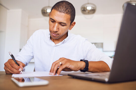 Man, paper and desk writing in planning, accounting or signing contract in home. Notebook, businessman and with a report, budget or finance on laptop, phone and page for business, goal or strategy