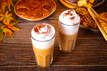 Pumpkin spice whipped latte in glasses. Hot autumn drink beverage. Nearby delicious pie and appetizers fruits and cheese.