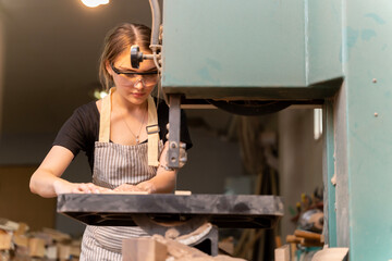 Portrait of a female carpenter using tools or machines for cutting, not drilling, wood to make furniture in a furniture factory. with modern tools