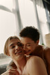 © LIGHTFIELD STUDIOS - Short haired woman smiling and hugging shirtless boyfriend at home.