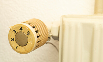 Closeup of old radiator heating in house with white wall background.  Knob with number to be adjust and control temperature in room in winter, energy bill expenses household