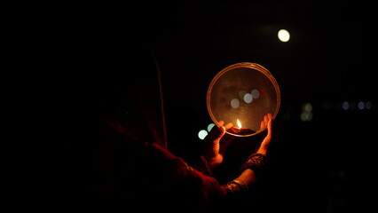 Woman hand holding Karwa Chauth strainer for the Karwa Chauth celebration on the night. Karwa Chauth strainer and Diya oil lamps for the Karwa Chauth celebration on the night