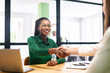 Happy female coworkers shaking hands in the office, african-american businesswoman smiling. Teamwork, partnerships and hiring concept