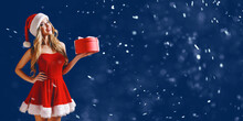 Woman Wearing Stylish Red Dress Of Christmas Costume Posing With Gift Box In Snow