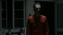 Man Wearing A Scary Mask Standing Behind A Young Woman In The Kitchen At Night. Horror Masked Killer In Orange Cloth Stalks His Victims. Halloween Festival Concept.