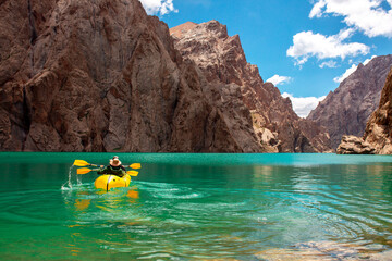 Wall Mural - Kayaking on a mountain lake. Two men are sailing on a red canoe along the lake along the rocks. The theme of water sports and summer holidays.