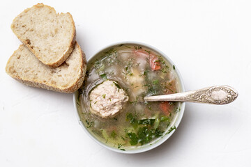 Wall Mural - Vegetable soup with meatballs in a plate on a white background. Two slices of bread side by side.