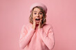 © Look! - Nice young caucasian lady holding hands on cheeks with mouth open is surprised on pink background. Blonde woman wavy hair wears beret and sweater. Shock concept
