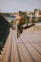 Wall Mural - Active young beautiful woman running on the promenade along the riverside