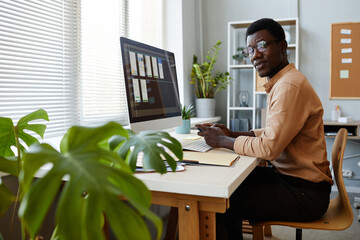 Wall Mural - Side view portrait of young black man looking at camera at office workplace decorated with plants