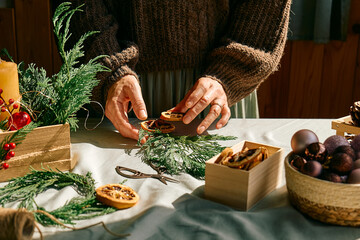 Wall Mural - Woman making Christmas arrangement with fir branches and dried oranges. Female hands creating Christmas craft handmade decor. New year celebration. Winter holidays.