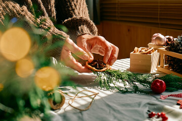 Wall Mural - Woman making Christmas arrangement with fir branches and dried oranges. Female hands creating Christmas craft handmade decor. New year celebration. Winter holidays.