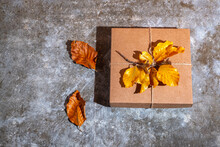 Craft Gift Box Decorated Autumn Leaves On A Gray Background. Thanksgiving And Zero Waste Concept.