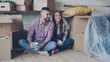 © silverkblack - Happy couple is sitting on floor in new house and having conversation discussing interior of their new home holding mugs. Carton boxes around them are in background.