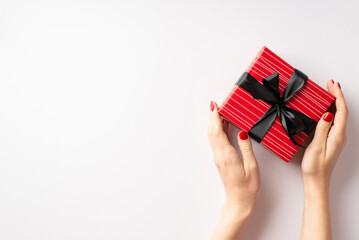 Wall Mural - Black friday sales concept. First person top view photo of girl's hands holding red giftbox with black ribbon bow on isolated white background with empty space