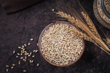 Wall Mural - Bowl of dry raw broken pearl barley cereal grain on dark background. Cooking pearl barley porridge concept.