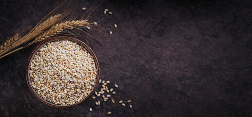 Wall Mural - Bowl of dry raw broken pearl barley cereal grain on dark background. Cooking pearl barley porridge concept.