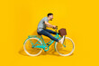 Side profile photo of young active energetic man driving new retro bicycle legs up crazy hurry fast speed look empty space isolated on yellow color background