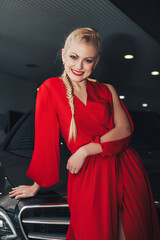 Pretty young woman model smiling and present car, newly automobile with bow at dealership. Happy woman in red dress with new auto with gold bow on roof. Car presents concept. Copy text space