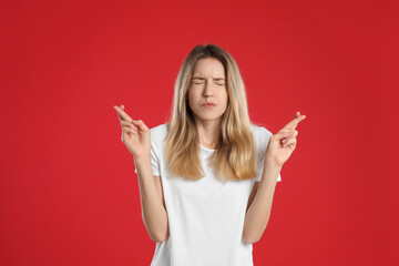 Wall Mural - Woman with crossed fingers on red background. Superstition concept
