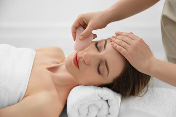 Young woman receiving facial massage with gua sha tool in beauty salon