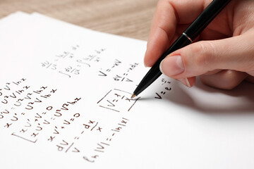 Student writing different mathematical formulas on paper, closeup