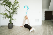 Businesswoman Sitting On The Floor In Office With Question Mark Above Her