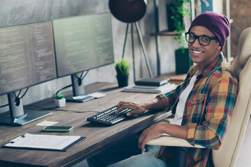 Photo of happy smiling freelancer wear hat glasses working instagram twitter facebook framework indoors workplace workstation loft