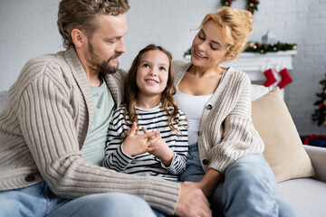 Smiling girl talking near parents on couch during new year at home