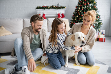 man looking at wife and daughter petting labrador during new year at home