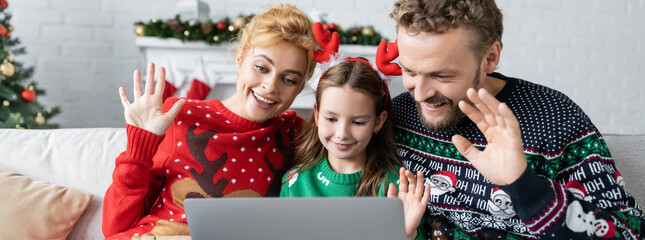 Wall Mural - Positive parents with daughter having video call on laptop during christmas at home, banner