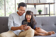 © aekkorn - Cute asian girl help young father show something on smartphone making selfie together, smart daughter and dad sit on couch hold mobile phone take family picture on moblie phone.